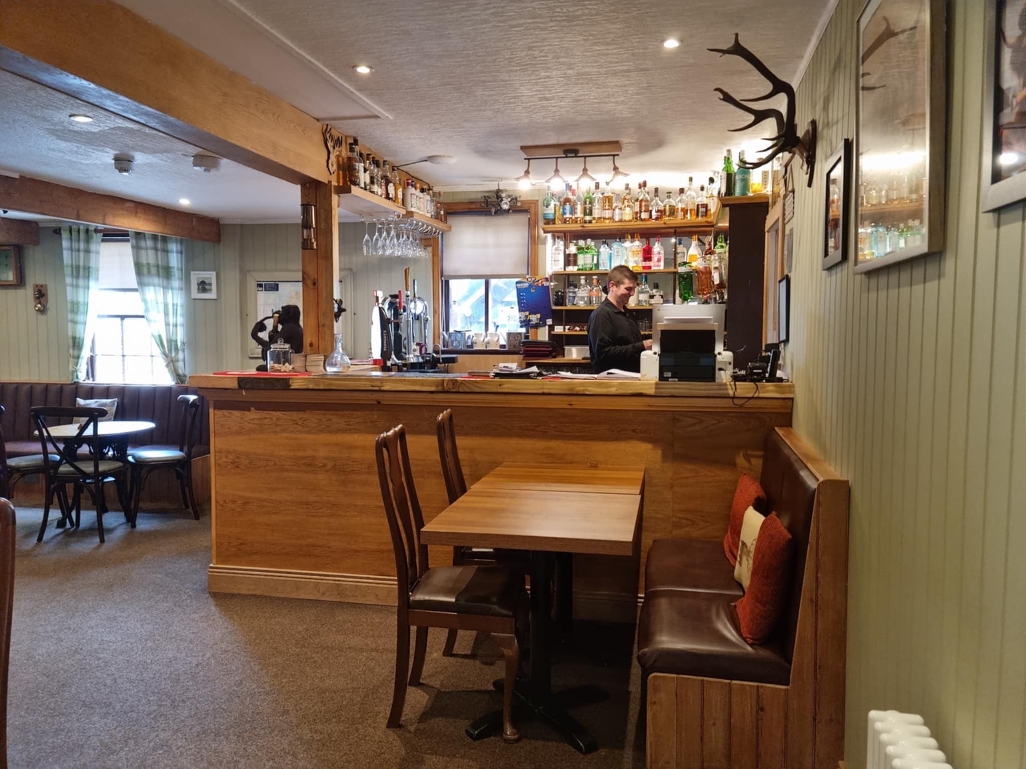 A bar area with wooden furniture, a counter, and shelves stocked with bottles.