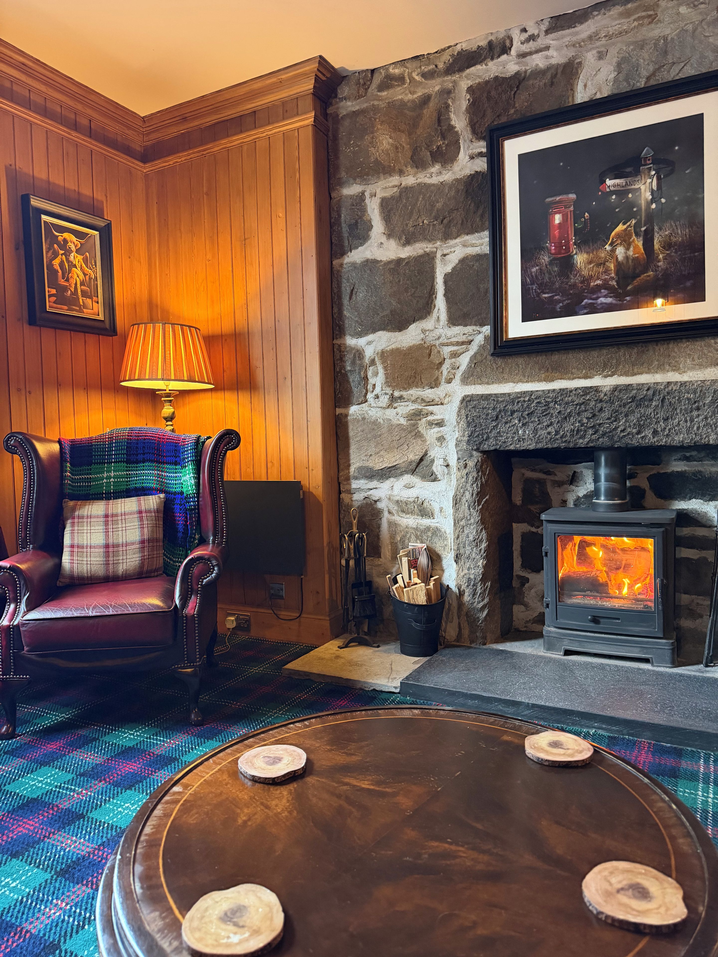 A cozy room with a stone fireplace, a leather armchair, a plaid blanket, and a framed picture on the wall.