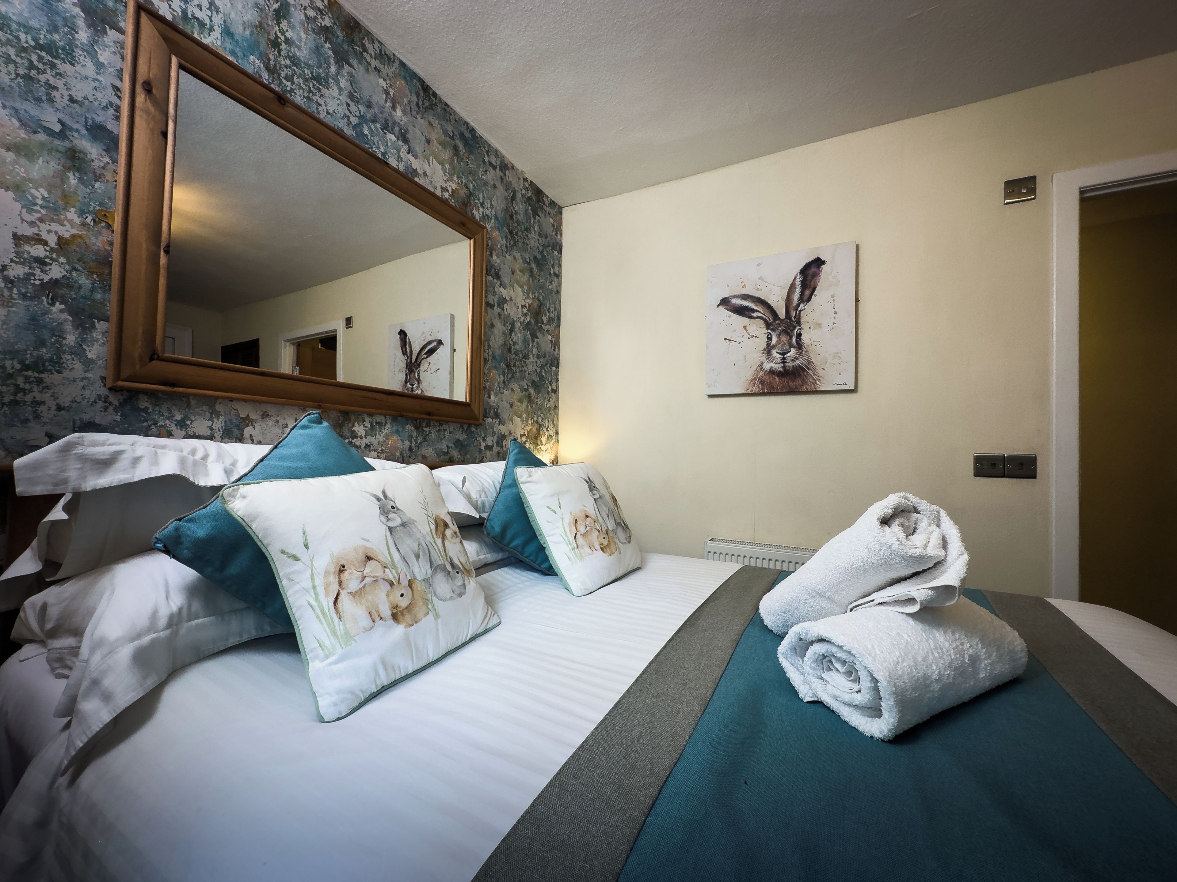 A hotel room with a large bed, a mirror, a painting, and a neatly made bed with towels.