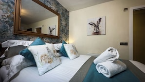 A hotel room with a large bed, a mirror, a painting, and a neatly made bed with towels. - Borgie Lodge Hotel (Thurso)