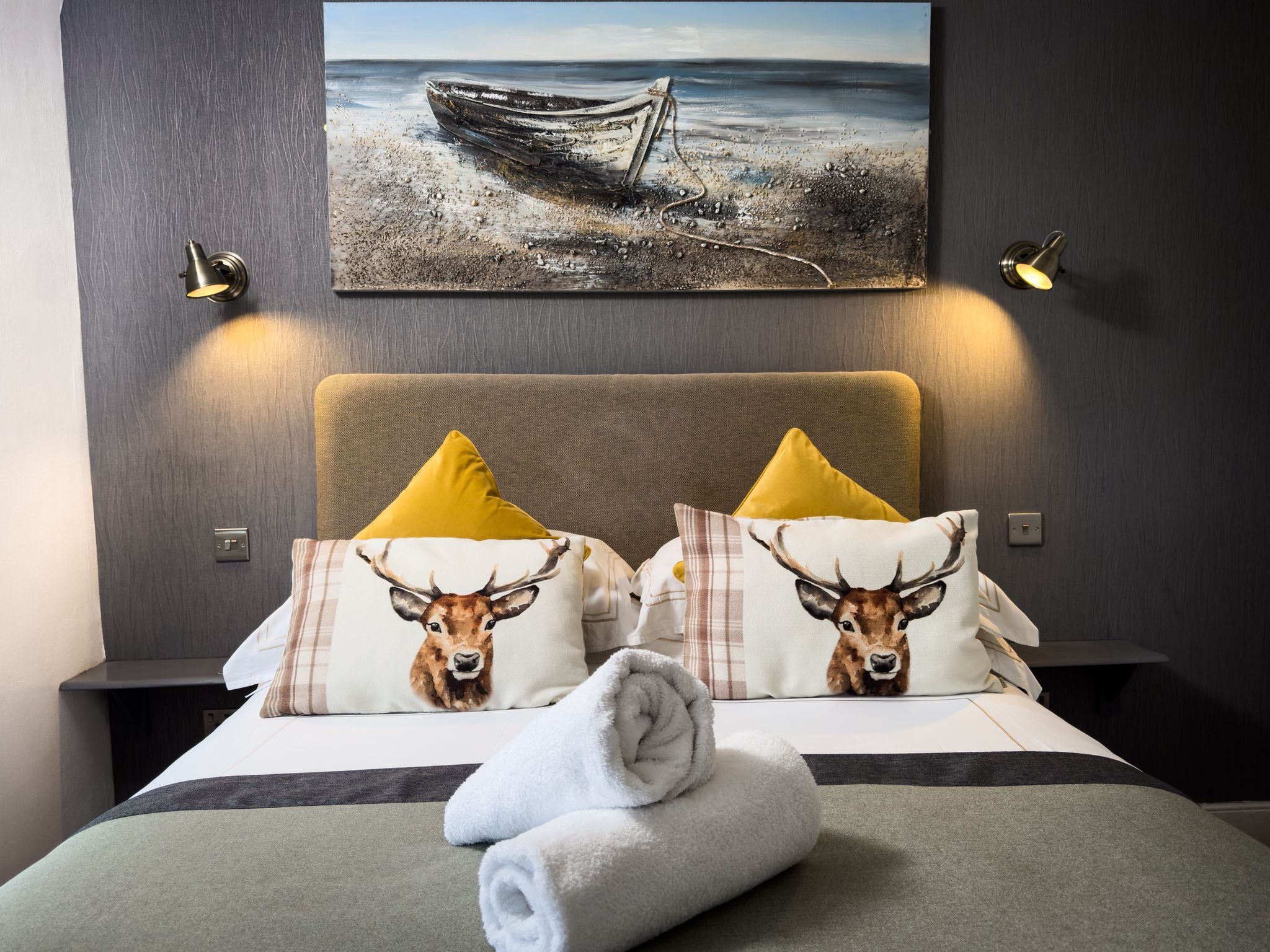 A hotel room with a bed, two nightstands, a painting of a boat on the wall, and two lamps.