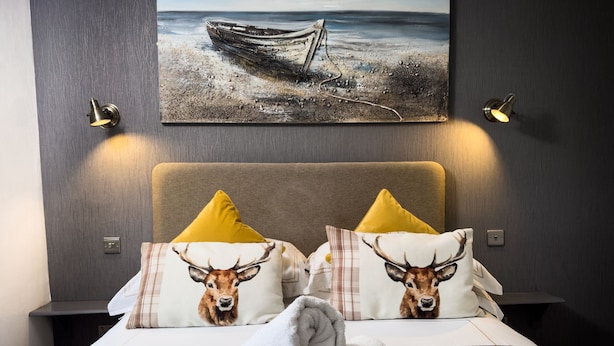 A hotel room with a bed, two nightstands, a painting of a boat on the wall, and two lamps. - Borgie Lodge Hotel (Thurso)