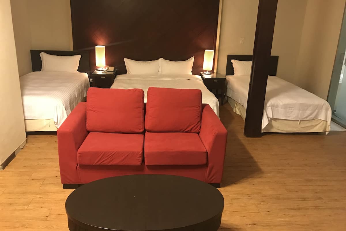 Habitación de hotel con dos camas, un sofá rojo, una mesa redonda y lámparas de noche.