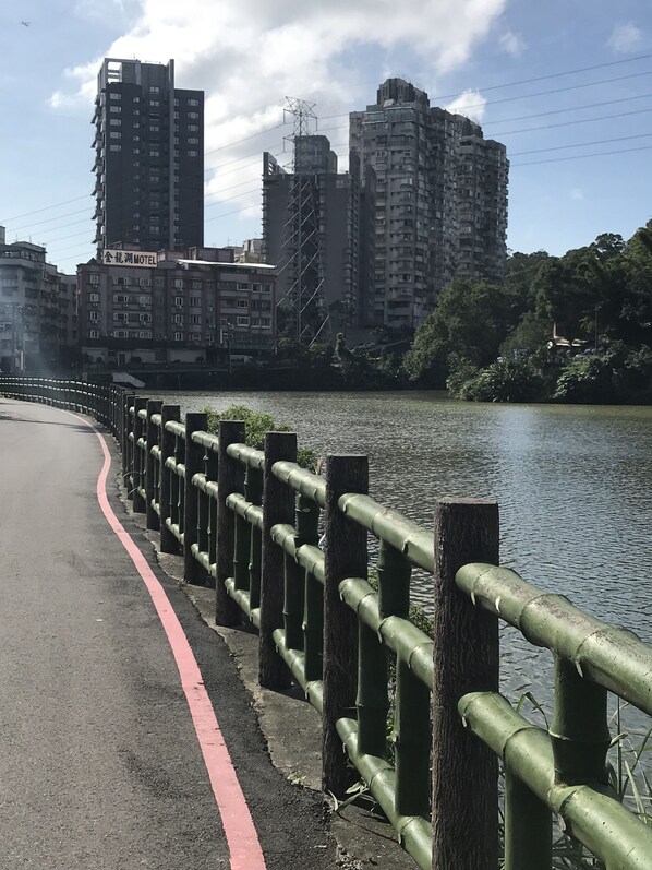 Un paseo fluvial con barandilla metálica, una línea roja que marca el sendero y un paisaje urbano con rascacielos al fondo.