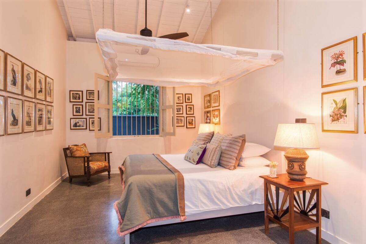 A bedroom with a bed, a nightstand, a chair, and a window with a view of greenery.