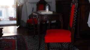Een kamer met een houten stoel met een rode kussen, een houten tafel, een spiegel en een kamerkleed met een patroon.