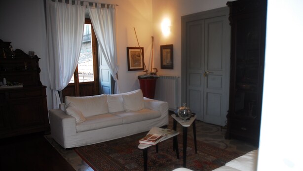 Een woonkamer met een witte bank, een salontafel, een vloerkleed, een houten kast en een deur.