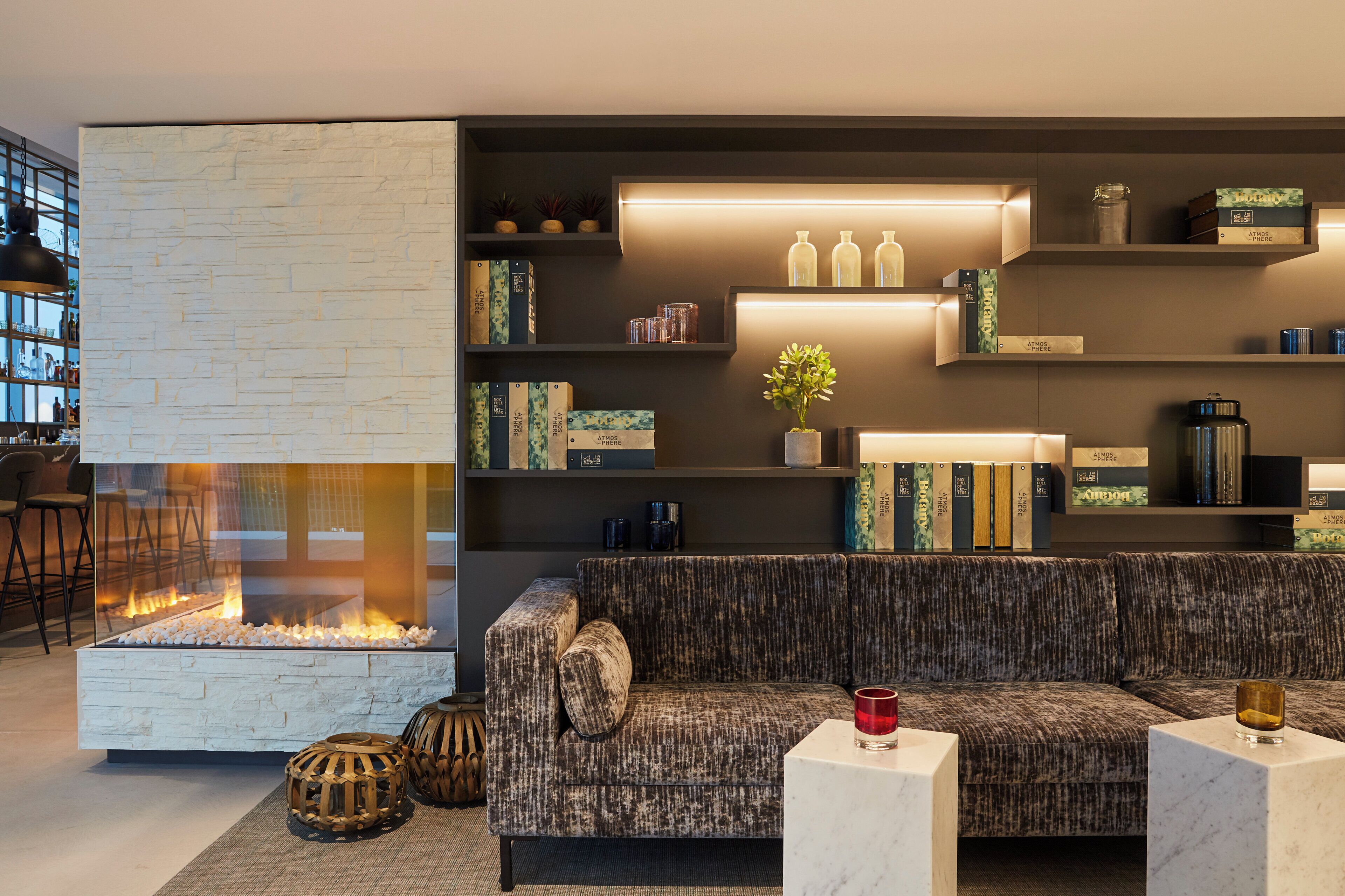 A modern living room with a stone fireplace, a sofa, and a bookshelf with decorative items.