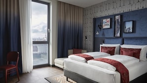 Una habitación de hotel moderna con una cama grande, una silla y vistas de la ciudad a través de un amplio ventanal.