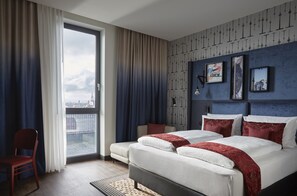 Una habitación de hotel moderna con una cama grande, una silla y vistas de la ciudad a través de un amplio ventanal.