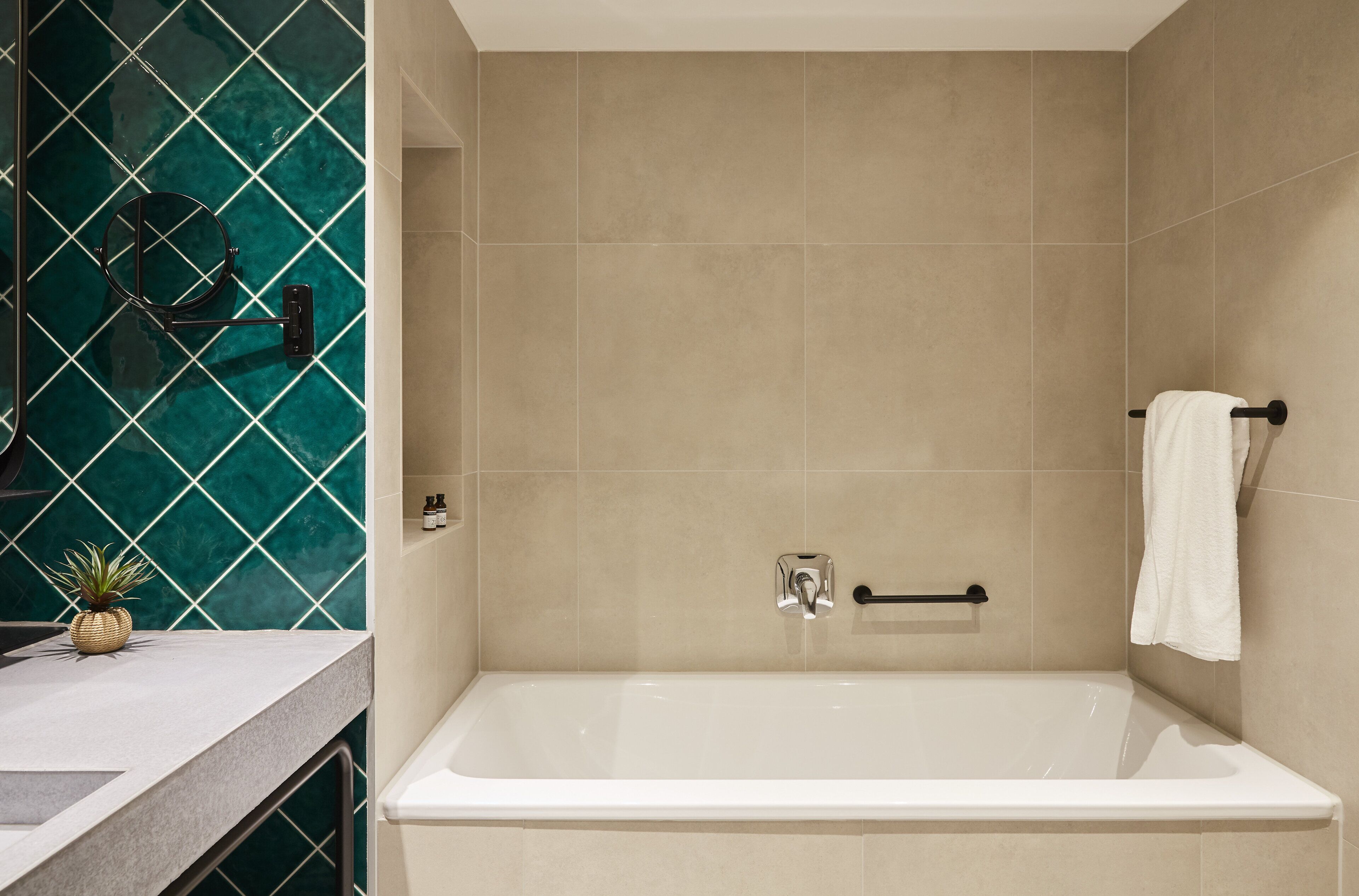 A modern bathroom with a bathtub, a towel rack, and a small plant on the counter.
