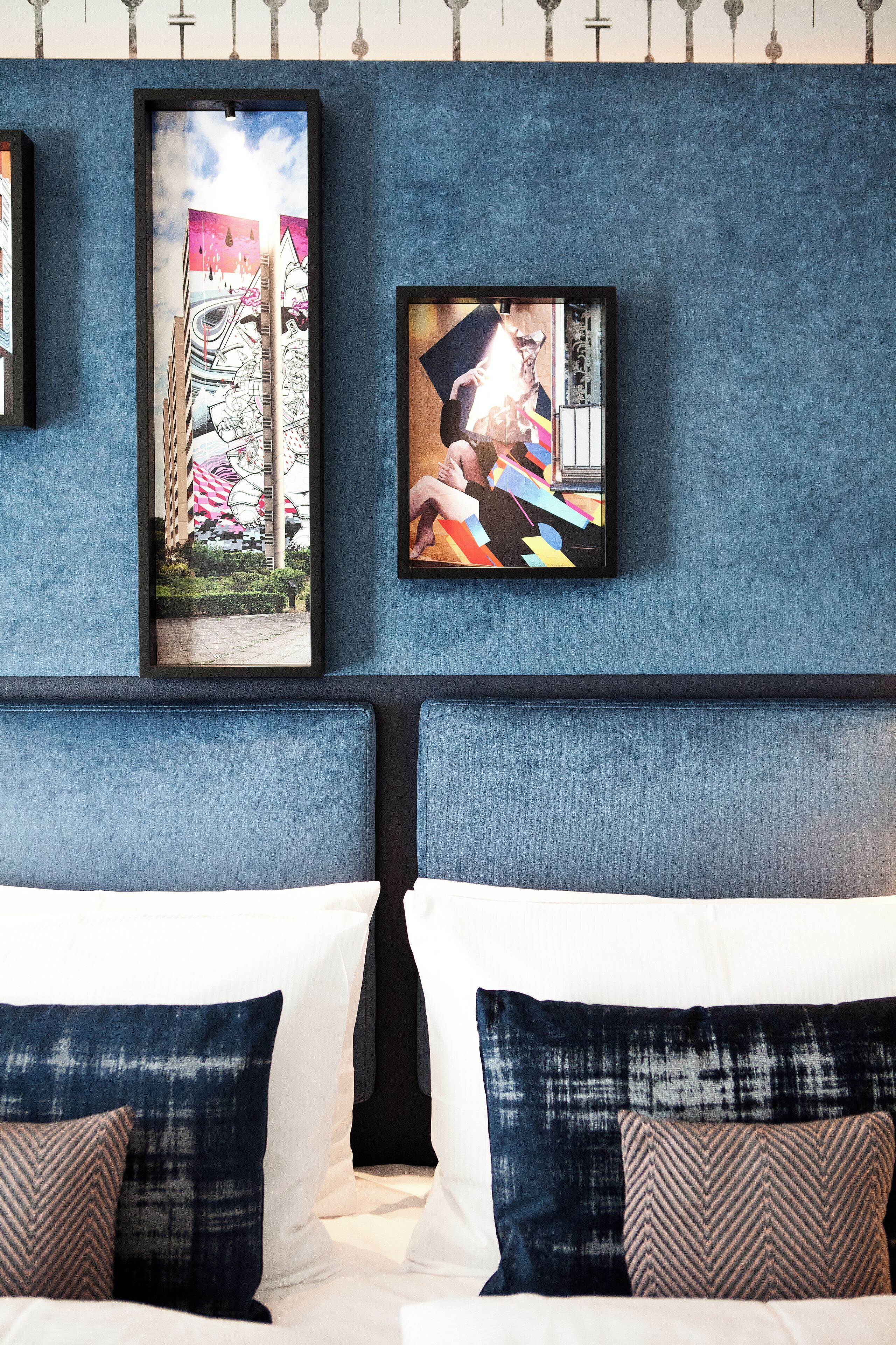 A hotel room with a large bed, two pillows, and two framed artworks on the wall.
