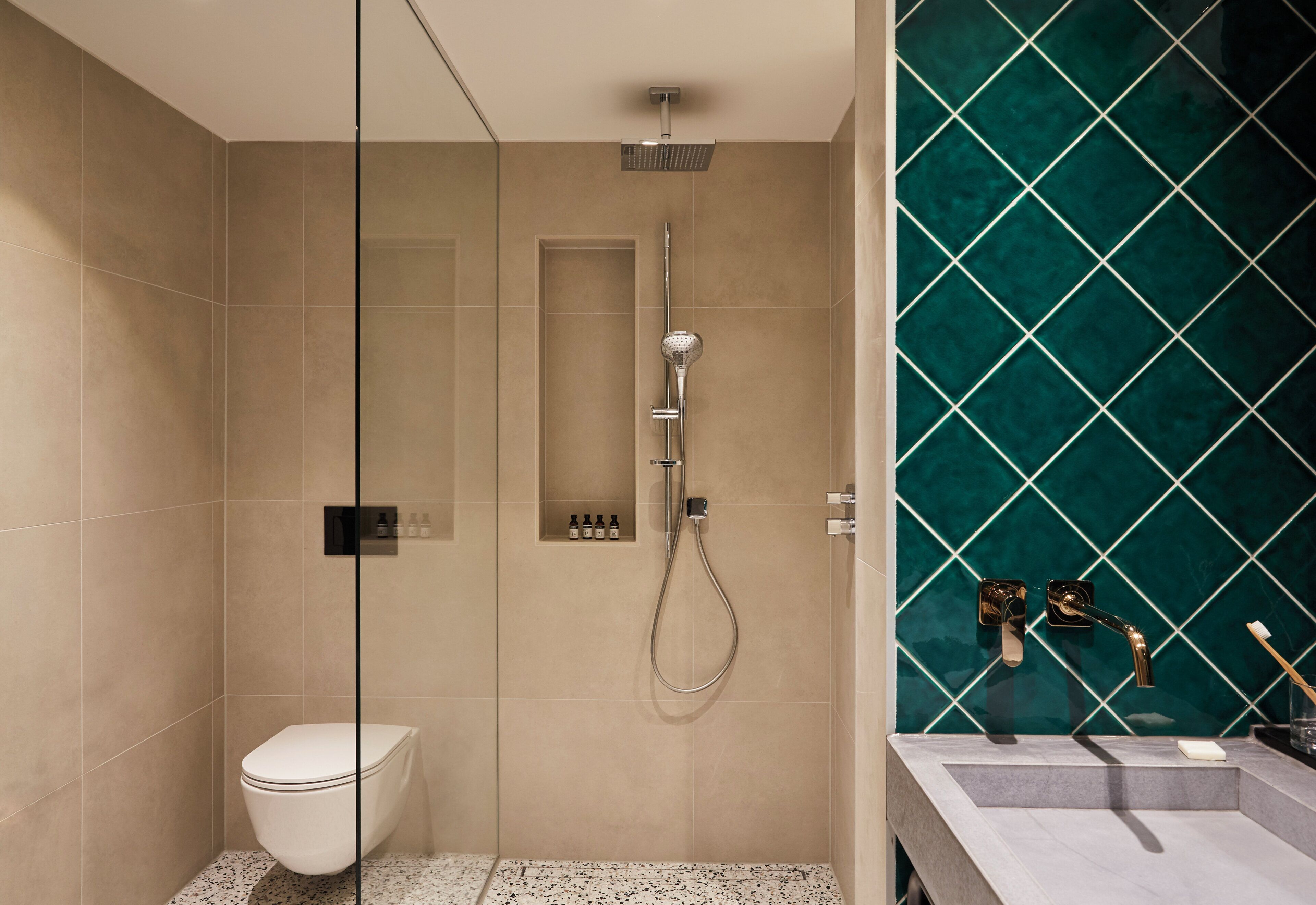 Un baño moderno con ducha envuelta en cristal, inodoro y lavamanos con salpicadero de azulejos verdes.