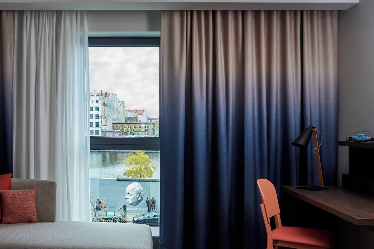 A hotel room with a large window, a bed, a desk, and a chair.