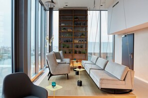 Un intérieur moderne avec un canapé, des fauteuils, une bibliothèque et une vue dégagée grâce à de grandes fenêtres.
