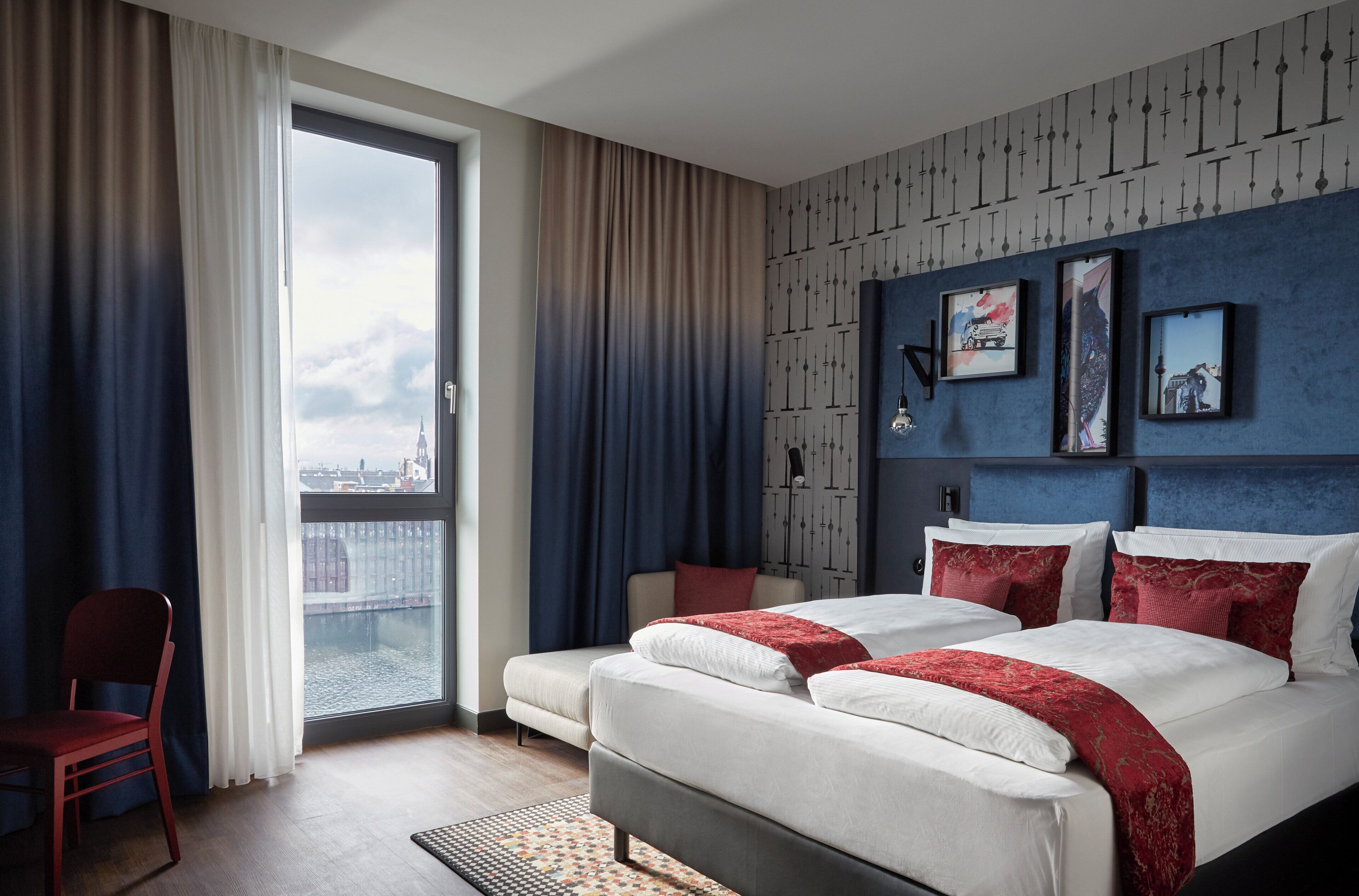 Ein Hotelzimmer mit einem großen Bett, einem Sessel und Blick auf die Stadt durch ein Fenster.