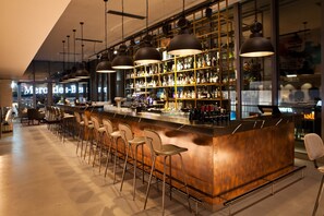 Un espace bar doté d’un long comptoir, de nombreux tabourets et de luminaires suspendus.