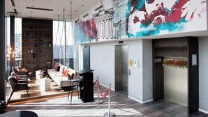 A modern hotel lobby with a long reception desk, seating area, and a mural on the wall. - Hotel Indigo Berlin - East Side Gallery by IHG (Berlin)