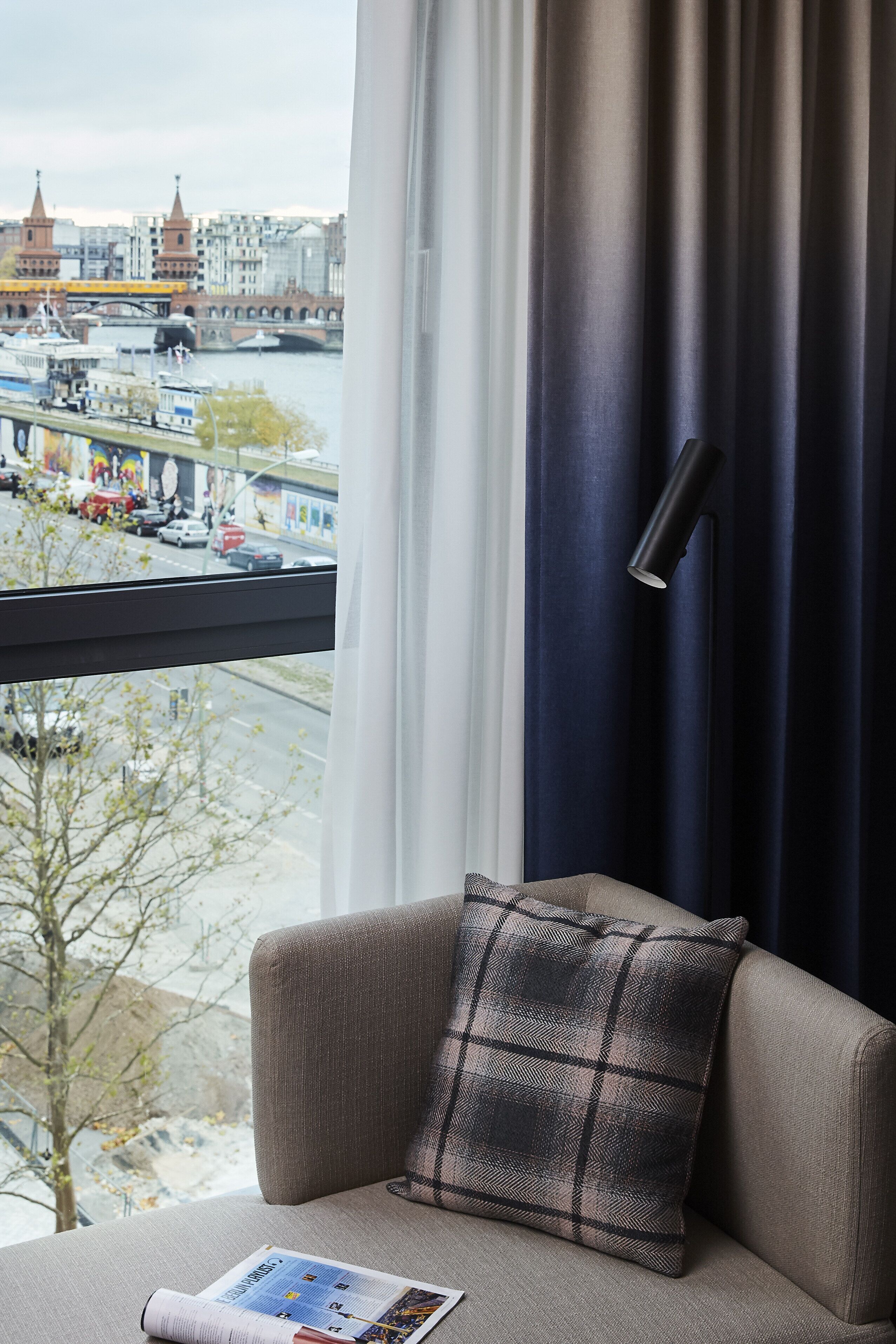 A room with a view of a cityscape, a sofa with a plaid pillow, and a black floor lamp.