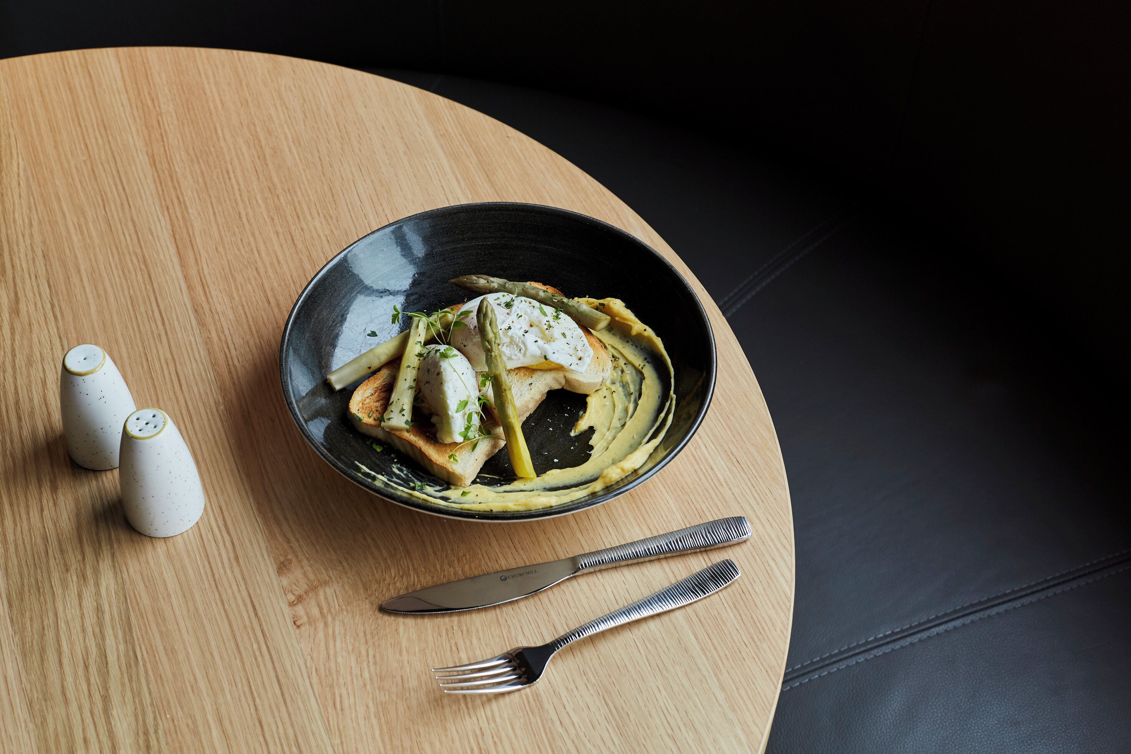 A black bowl with a creamy sauce and vegetables on a wooden table.