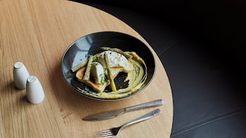 A black bowl with a creamy sauce and vegetables on a wooden table.