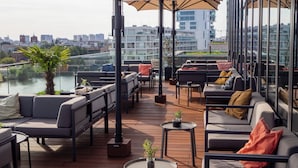 Una terraza en la azotea con mesas al aire libre, vistas de la ciudad y un río.