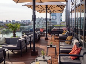 Una terraza en la azotea con mesas al aire libre, vistas de la ciudad y un río.