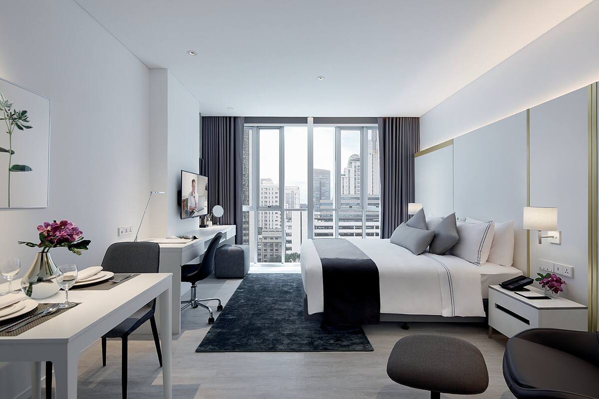 Ein modernes Hotelzimmer mit einem großen Bett, einem Schreibtisch, einem Sessel, einem Fernseher und Blick auf die Stadt.