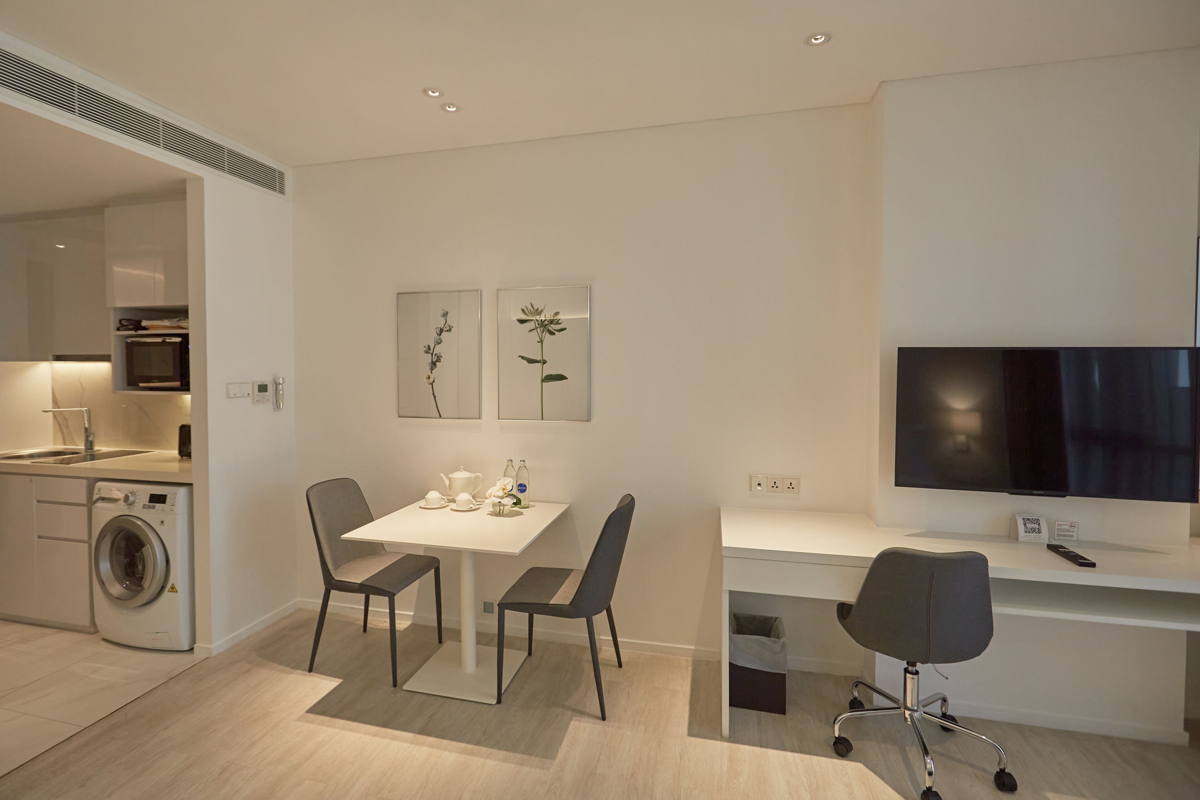 A modern kitchen with a built-in washing machine, a dining area with a table and chairs, and a TV on a desk.