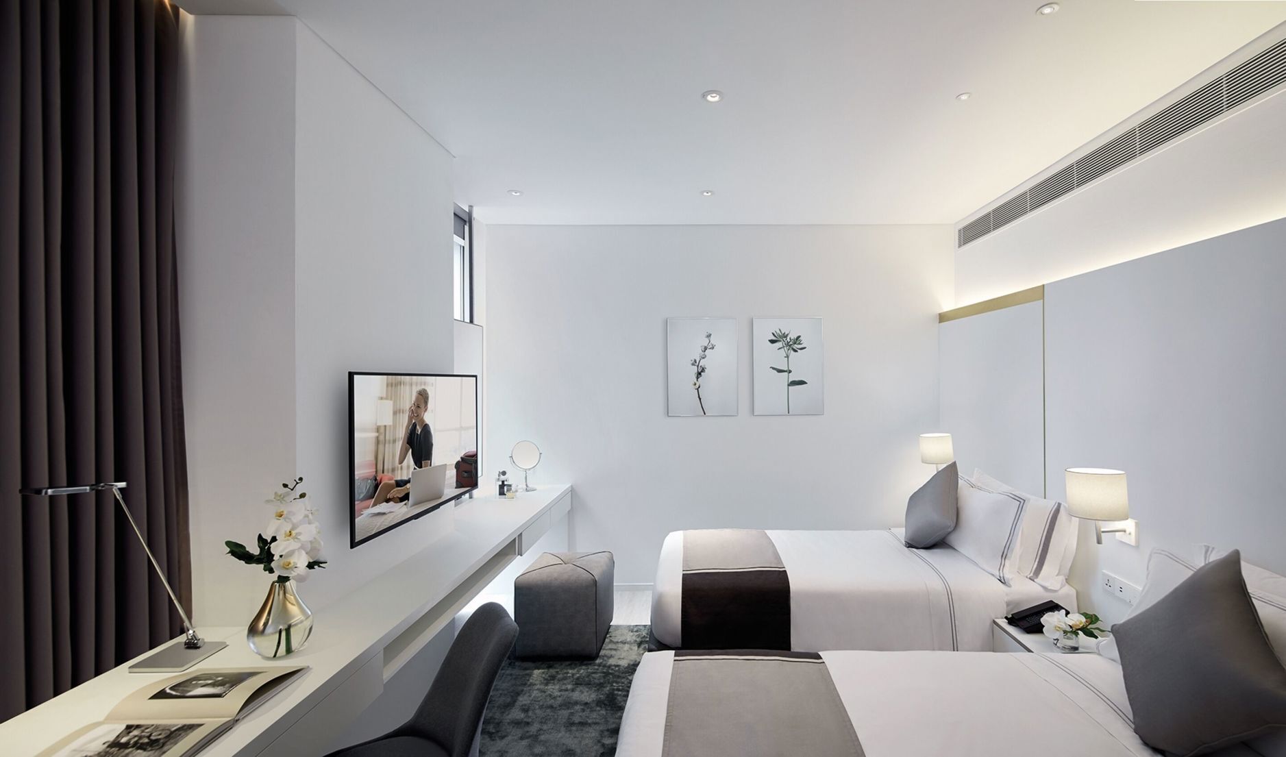 Ein modernes Hotelzimmer mit Bett, Nachttischen, Schreibtisch, Sessel und Spiegel. Kunstwerke zieren die Wand.