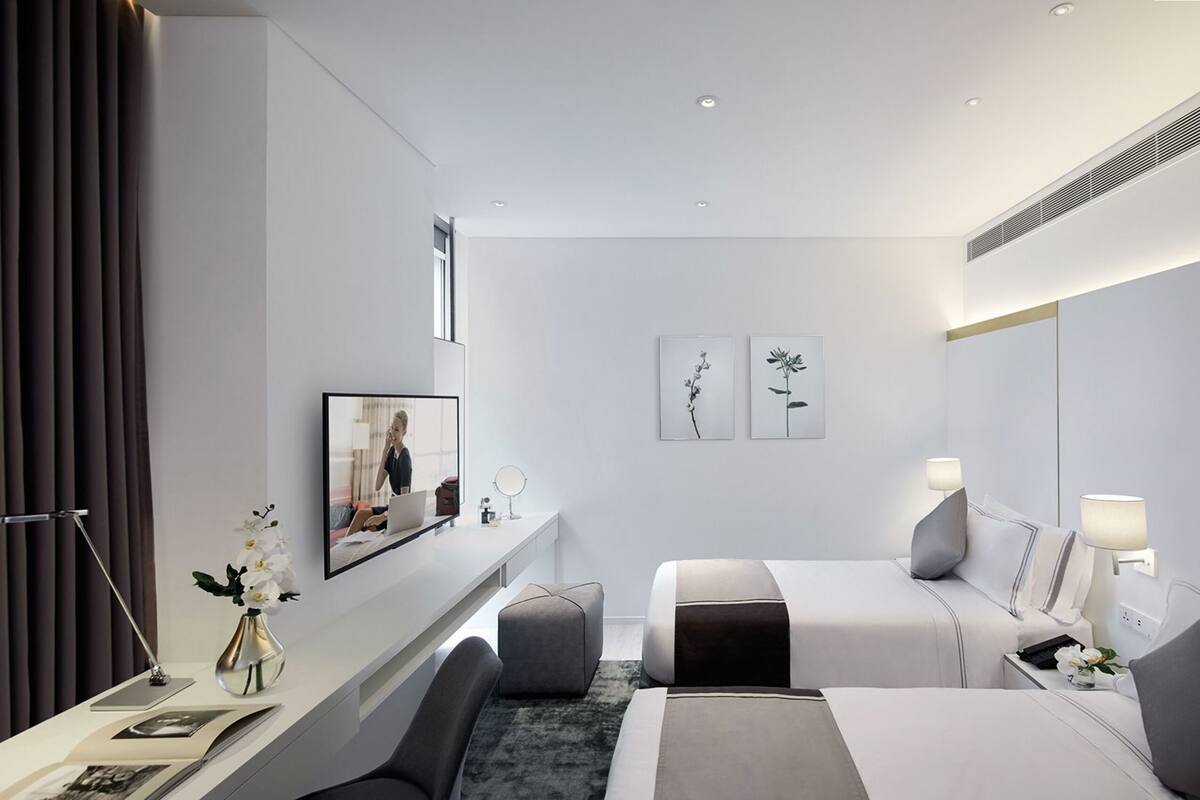 Ein modernes Hotelzimmer mit Bett, Nachttischen, Schreibtisch, Sessel und Spiegel. Kunstwerke zieren die Wand.