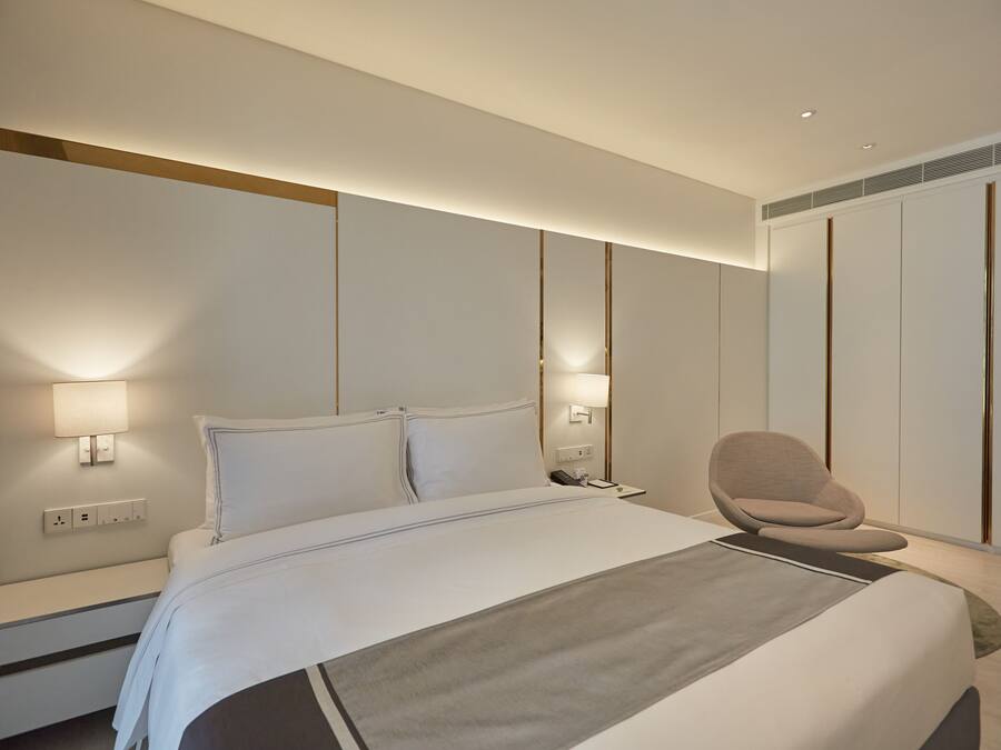 A modern hotel room with a large bed, bedside lamps, a chair, and a wardrobe.