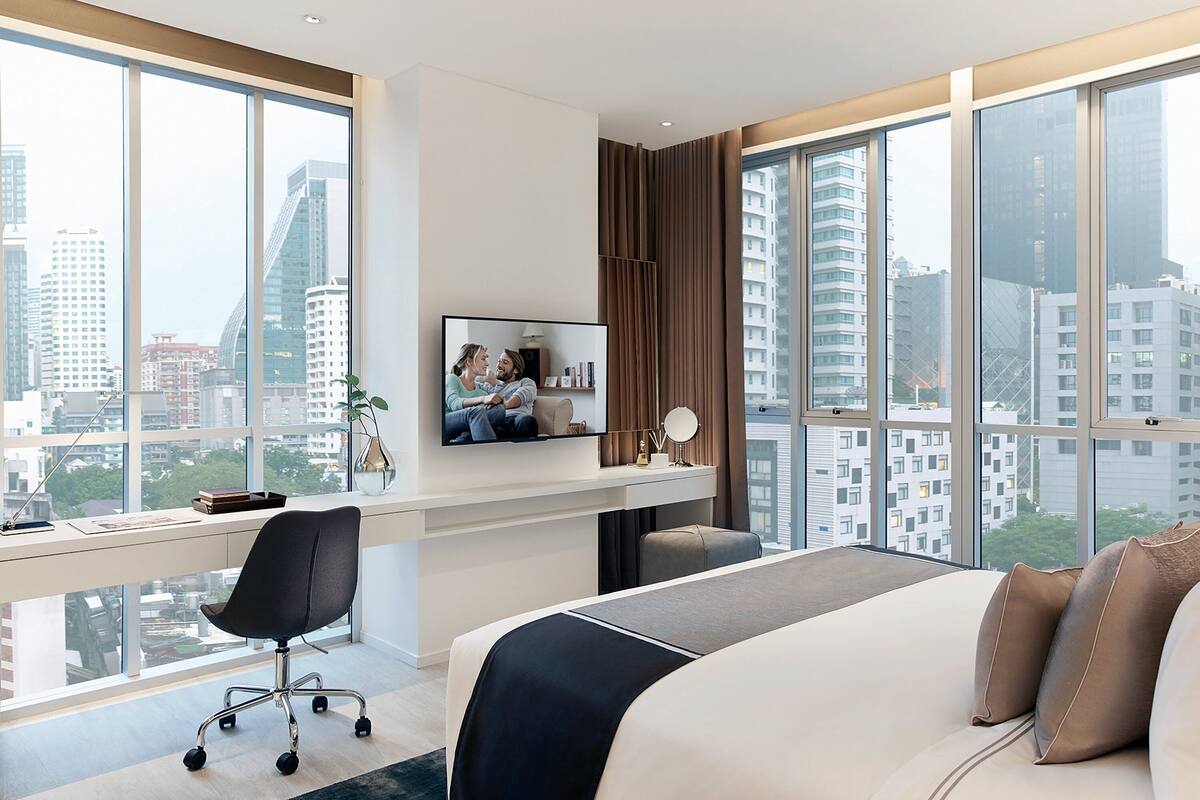 Ein modernes Hotelzimmer mit einem großen Bett, einem Schreibtisch mit Computer und einem Fernseher.