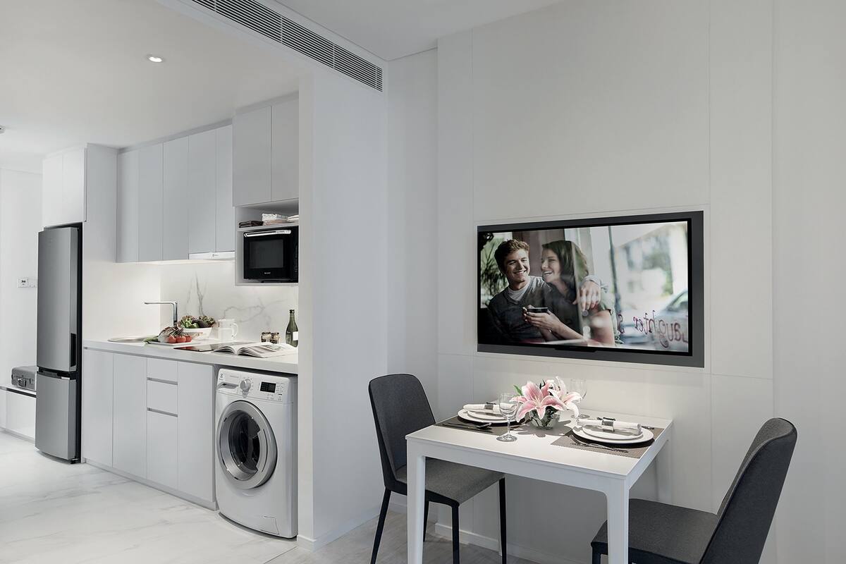 Eine moderne Küche mit Einbauwaschmaschine und -trockner, einem Essbereich mit Tisch für zwei Personen und einem an der Wand befestigten Flachbildfernseher.