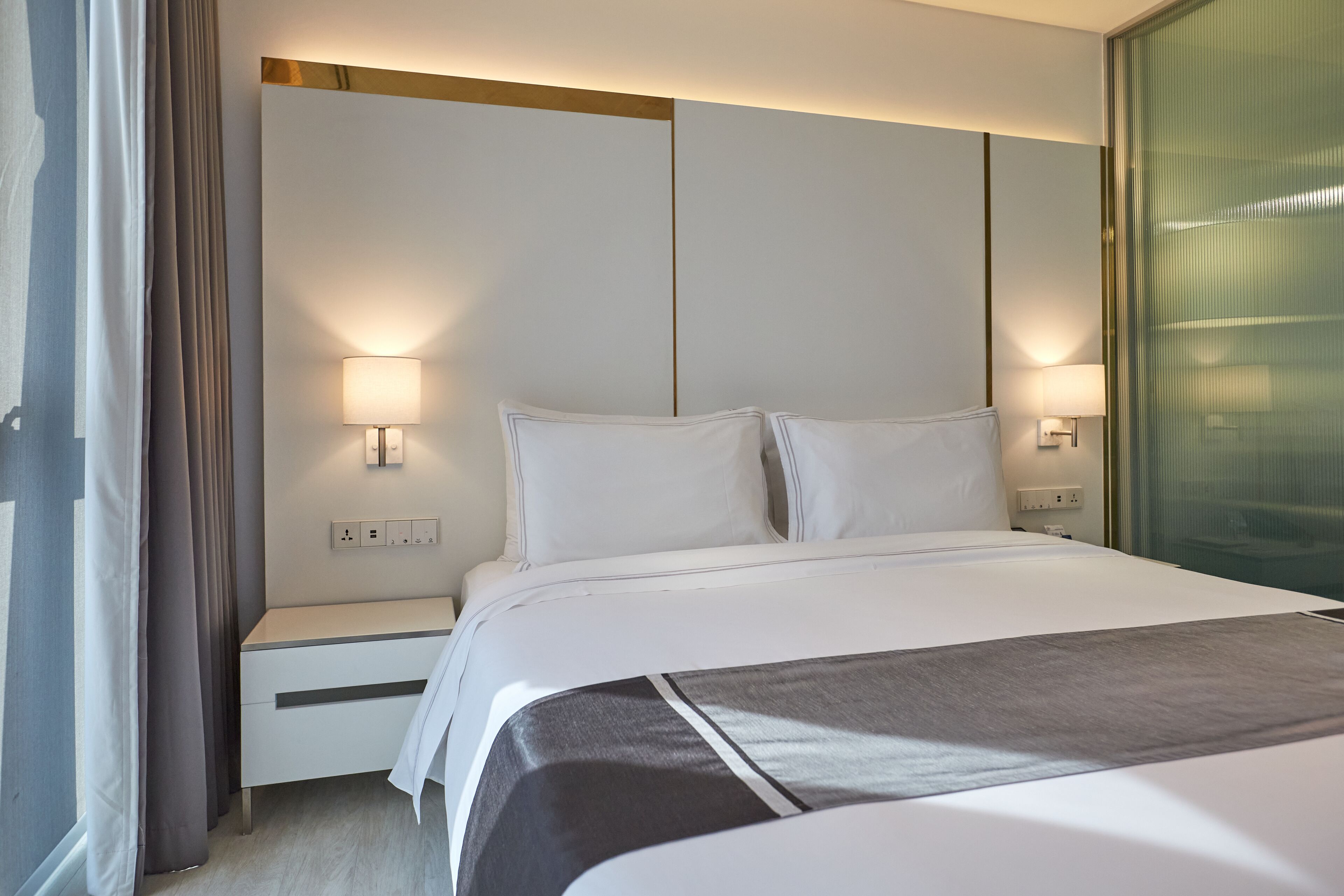 A modern hotel room with a large bed, bedside tables, and wall-mounted lamps.