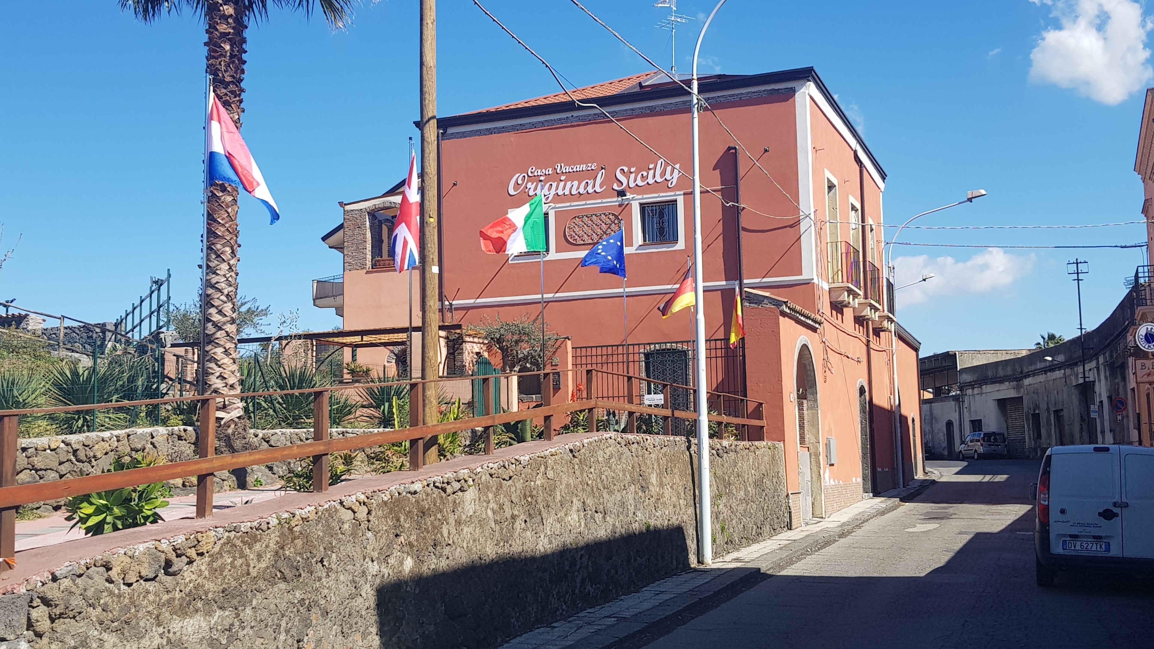 Een gebouw met een bord waarop "Casa Vacanze Original Sicily" staat en verschillende vlaggen, waaronder de Italiaanse vlag.