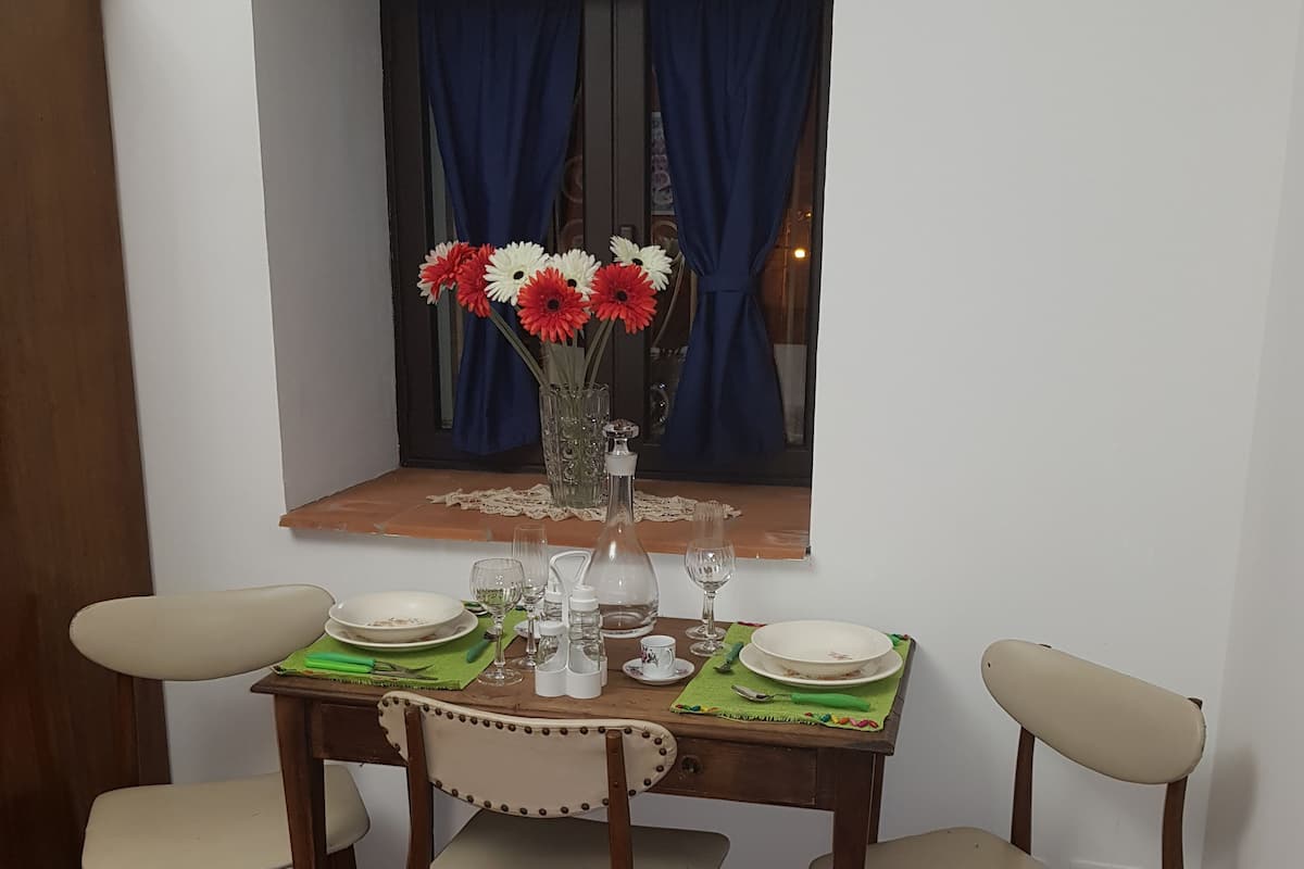 A dining table with four chairs, a vase with flowers, and a window with curtains.