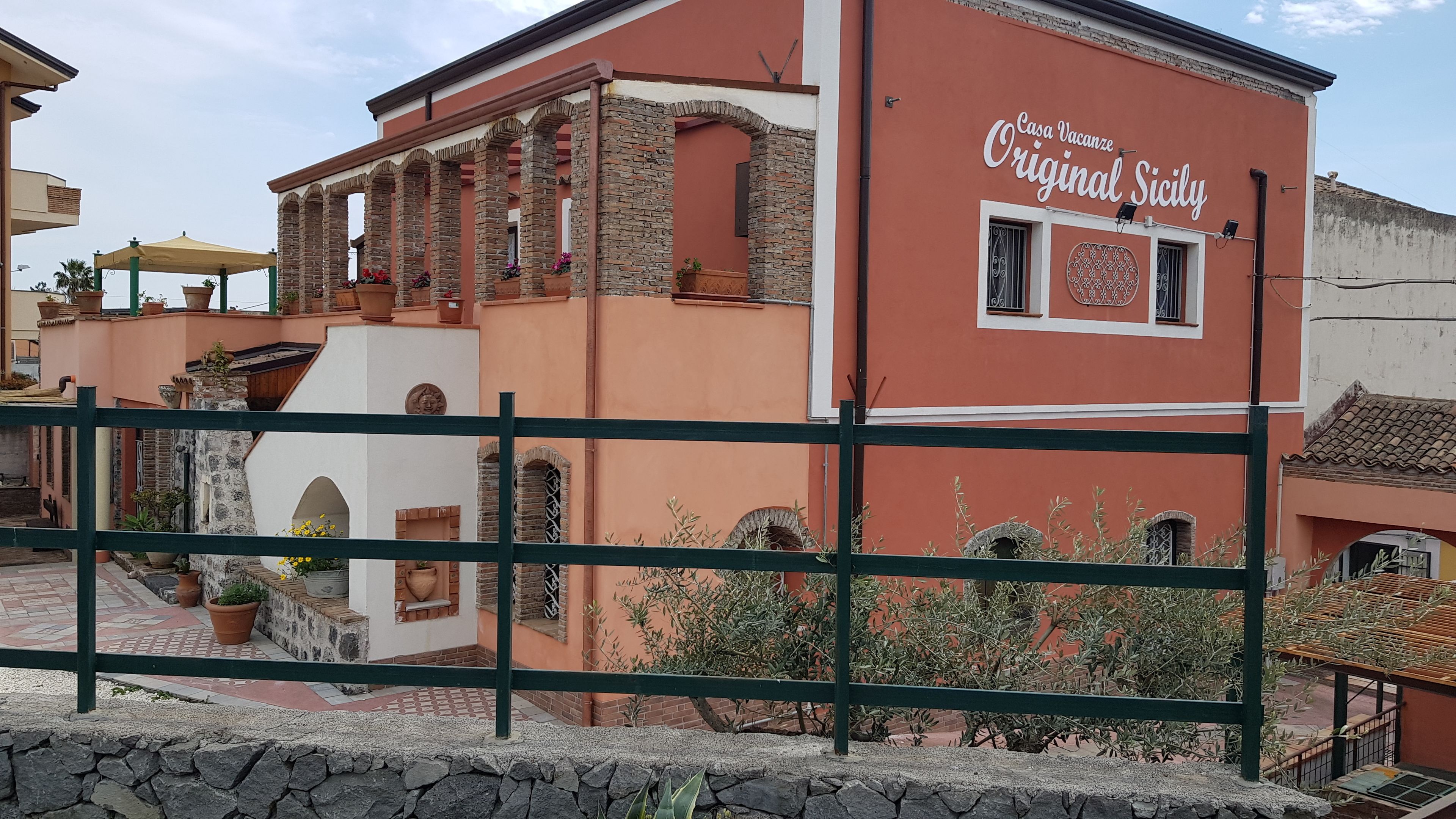 A building with a sign reading "Casa Vacanze Original Sicily," featuring stone arches and a tiled roof.