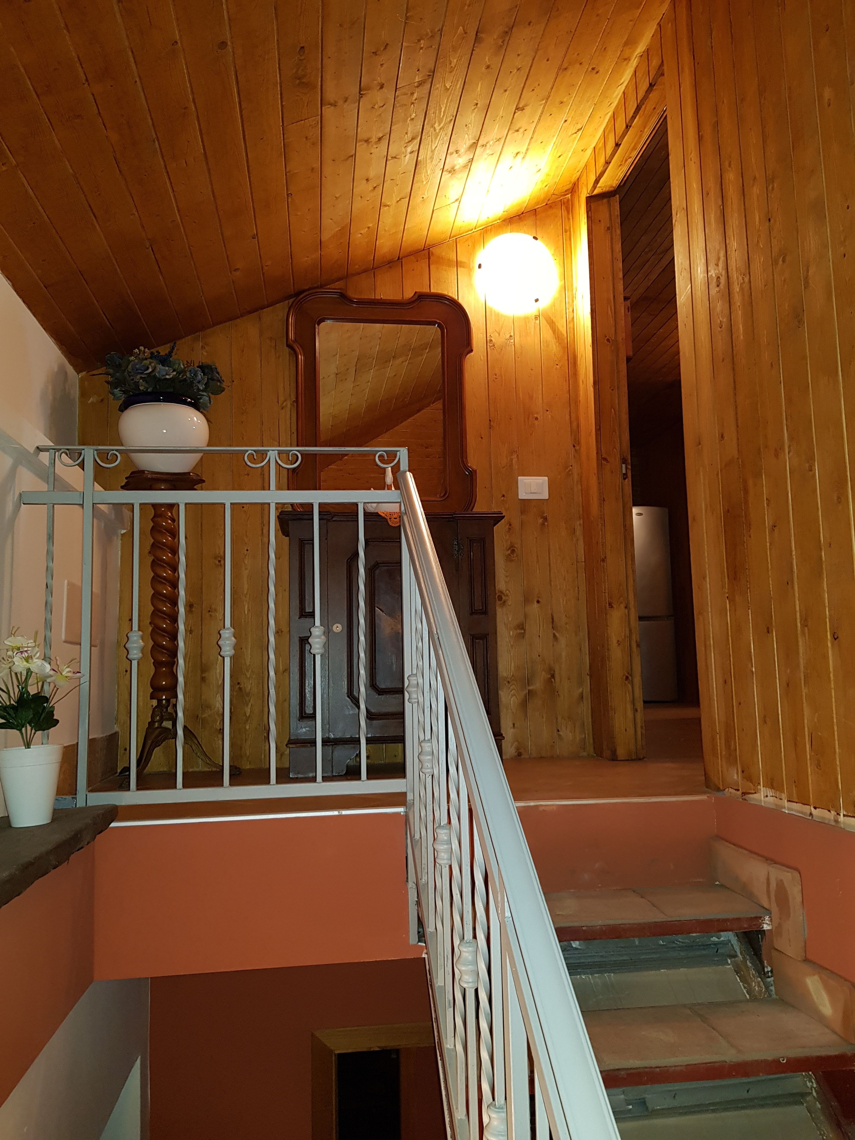 Un escalier en bois avec une rampe, un pot de fleurs et un luminaire.