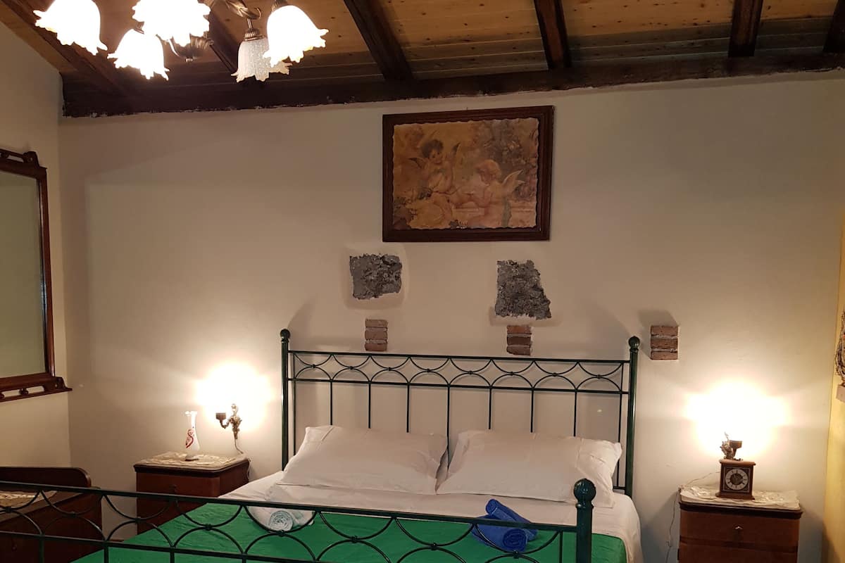 A bedroom with a green bedspread, a wooden headboard, a painting, and a chandelier.