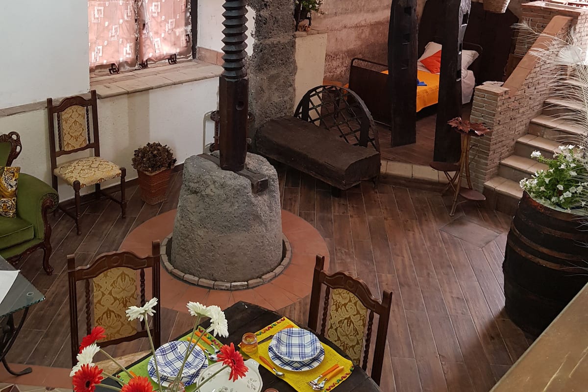 A dining area with a stone centerpiece, wooden chairs, a table set for four, and a staircase leading to an upper level.