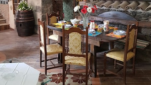 Uma área de refeições rústica com uma mesa de madeira posta para quatro pessoas, rodeada por paredes de pedra e um teto abobadado.