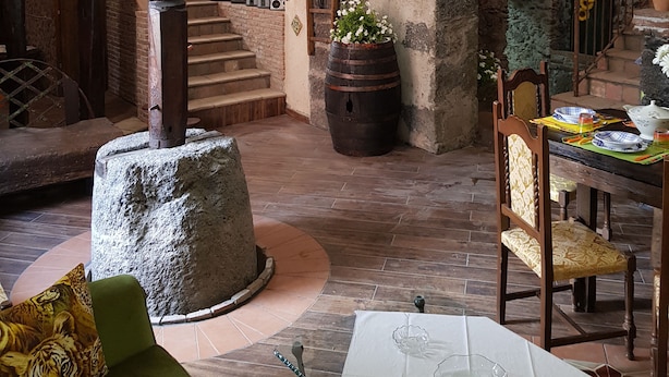 Interior rústico com paredes de tijolos aparentes, uma coluna de pedra, uma escada de madeira e uma área de refeições com uma mesa posta para dois.