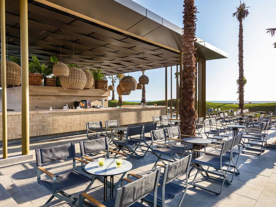 An outdoor dining area with tables and chairs, a bar with wicker baskets, and palm trees.