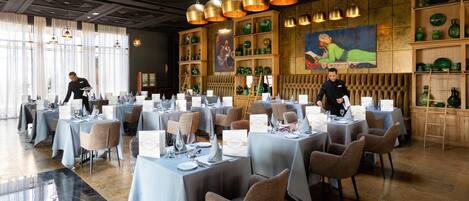 A restaurant with multiple tables set for dining, a bartender preparing drinks, and a large mural on the wall.