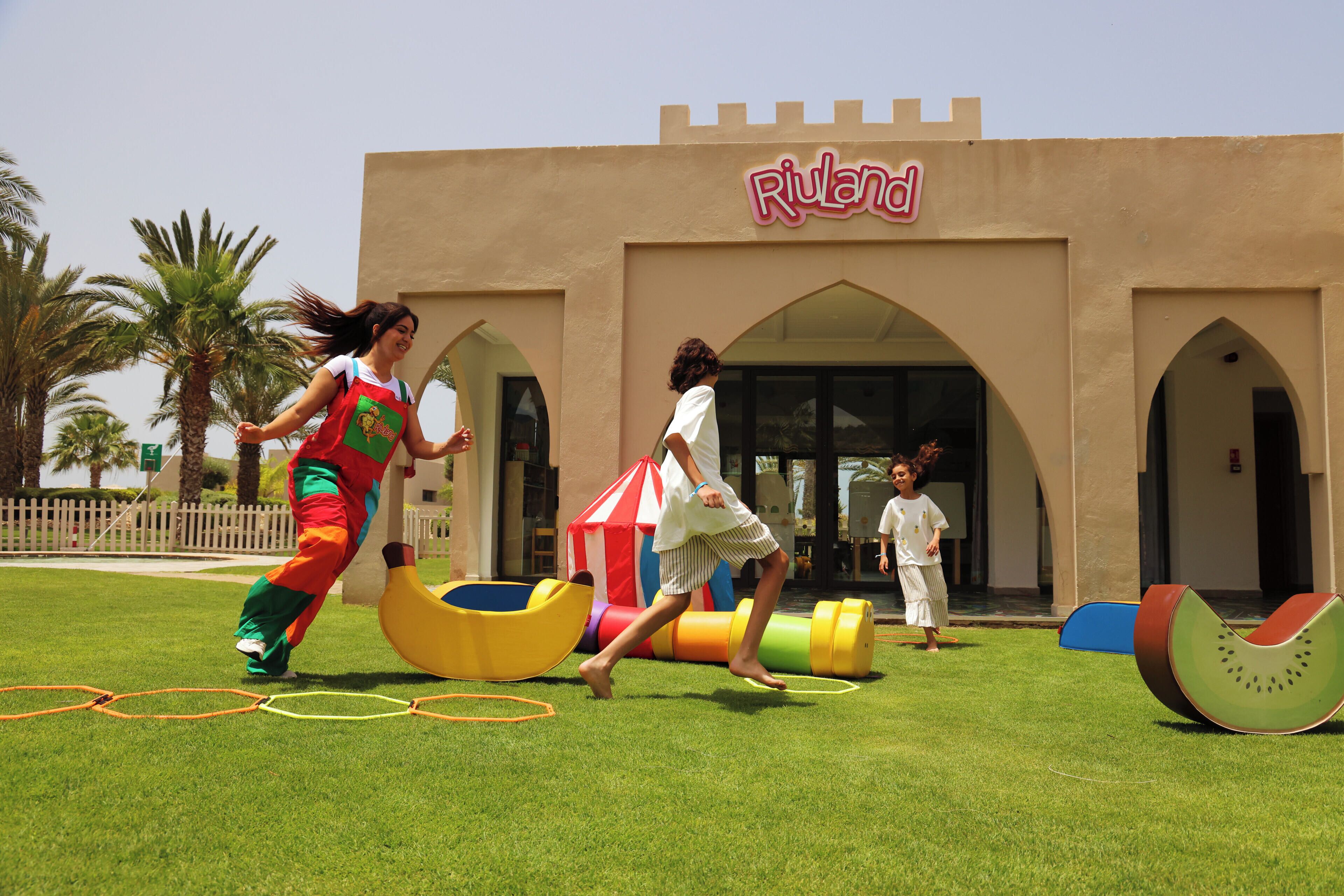A playground with a castle-themed play structure and a building with 'Riuland' signage.