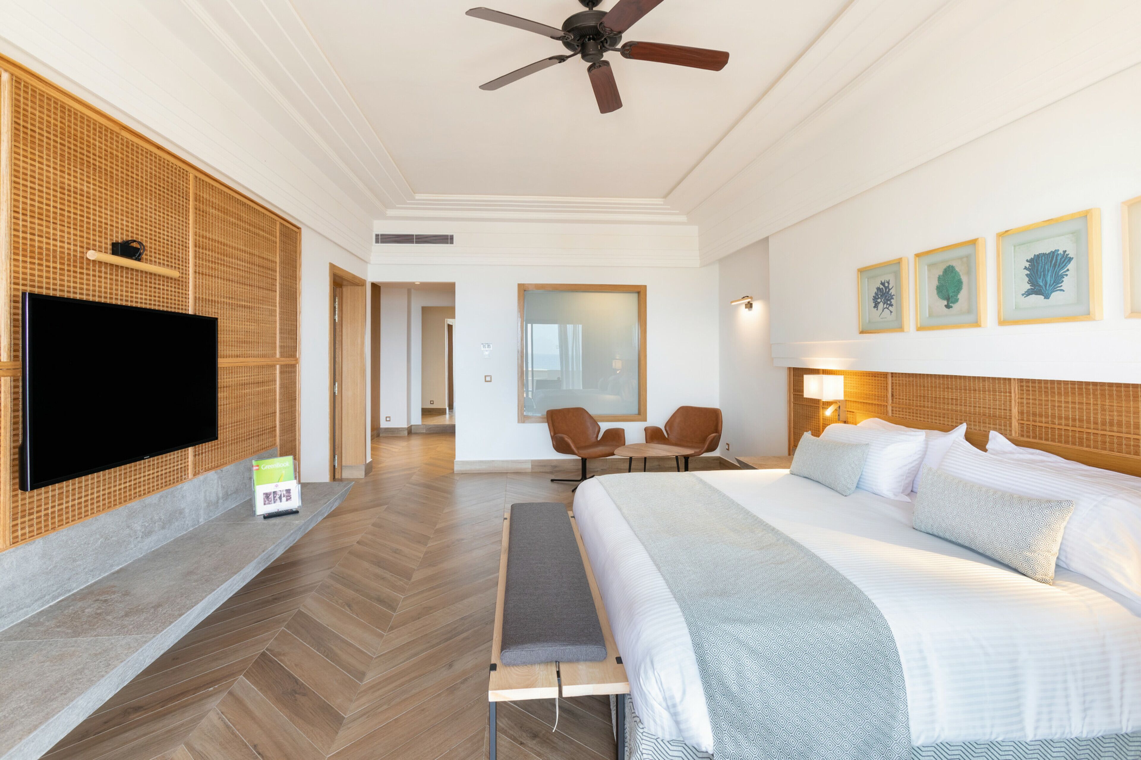 Ett hotellrum med en stor säng, en platt-TV, en takfläkt och en sittgrupp med stolar.