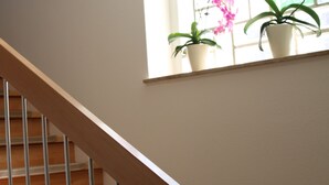 A wooden staircase with a handrail, leading to a landing with a window overlooking a balcony with potted plants. - Hotel Moerser Hof (Moers)