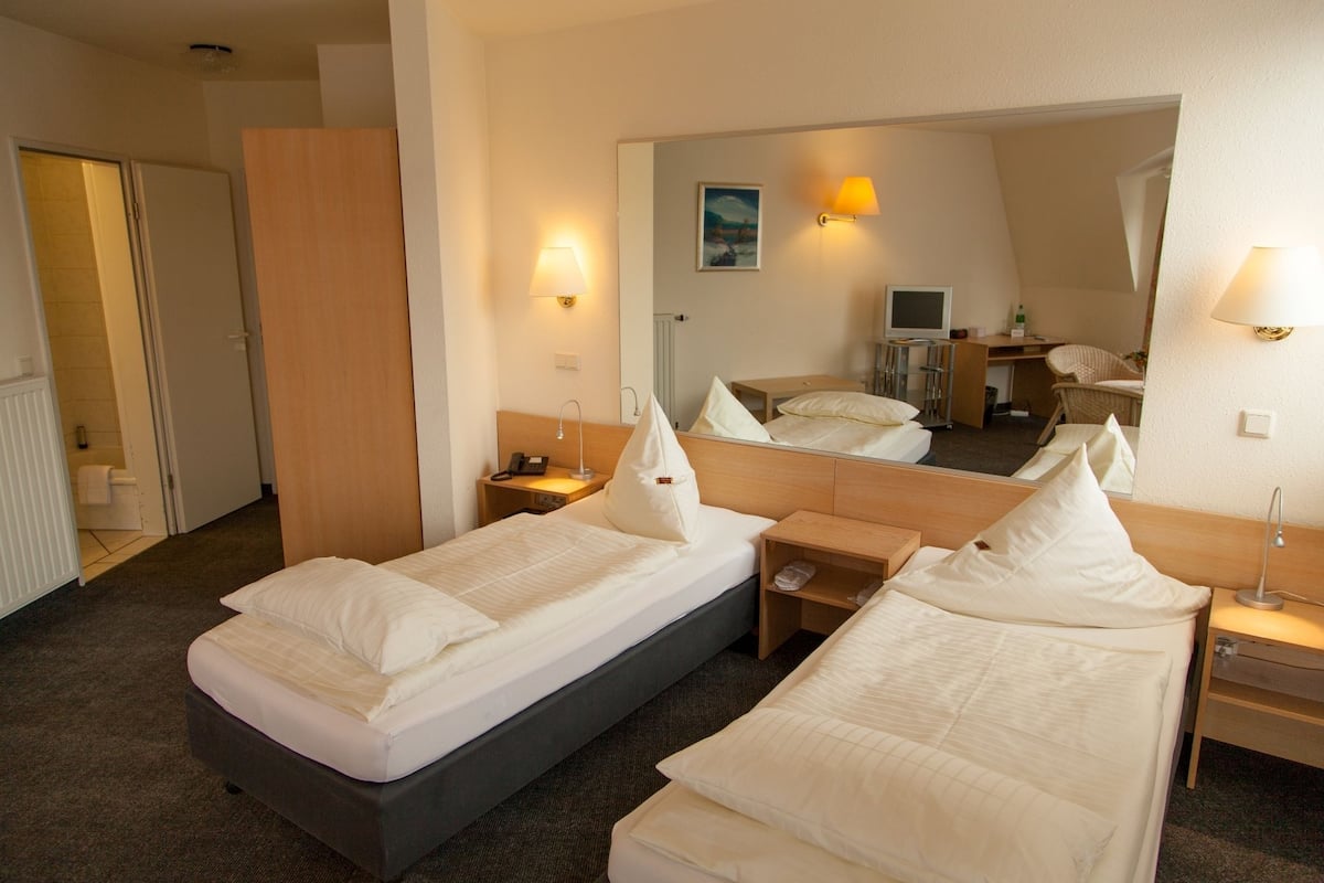 A hotel room with two single beds, a desk, a chair, a mirror, and a small TV.