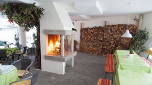 An outdoor dining area with a fireplace, wooden logs, and metal chairs. - Hotel Moerser Hof (Moers)